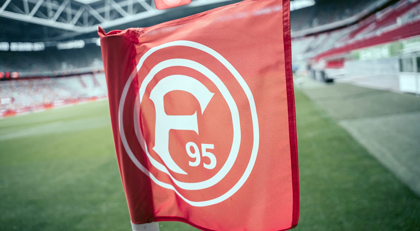 Eine rote Fahne mit dem Fortuna Düsseldorf-Logo und der Zahl 95 vor dem Hintergrund eines Fußballstadions.